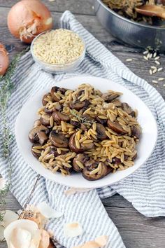 a white plate topped with mushroom pasta next to two bowls filled with mushrooms and onions