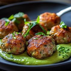 some meatballs with green sauce on a black plate