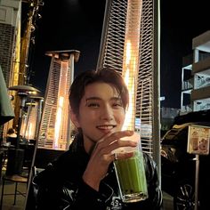 a young man holding a green smoothie in front of a tall building at night