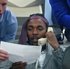 a man is sitting in an office chair talking on the phone and holding papers to his ear