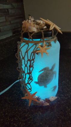 a mason jar with sea shells and starfish in it on a counter top next to a string light