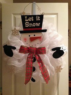 a snowman door hanger decorated with white tulle and red plaid bow, says let it snow