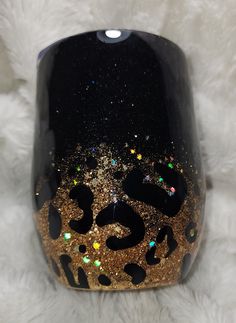 a black vase with gold glitter and leopard print on the side, sitting on a white furnishing