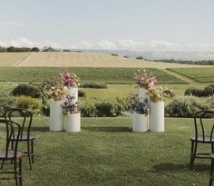 two tall white vases with flowers are on the grass near some chairs and tables