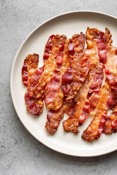 bacon strips on a white plate sitting on a gray counter top next to a fork and knife