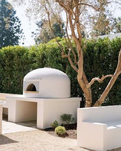 an outdoor pizza oven sitting on top of a white bench next to a small tree