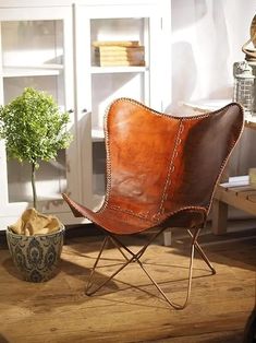 a brown leather chair sitting on top of a wooden floor next to a potted plant