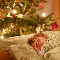 a little boy sleeping in bed next to a christmas tree