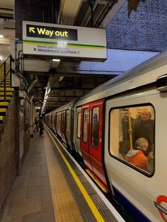 a subway train pulling into a station with people on the platform and stairs leading up to it