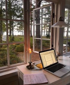 an open laptop computer sitting on top of a desk next to a candle and window