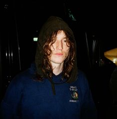 a man with long hair wearing a hoodie and looking into the camera at night