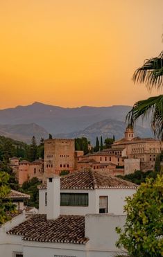 the sun is setting over an old town with mountains in the backgrouds