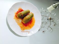 two pickles on a white plate with sauce