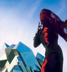 a woman standing in front of a building wearing a black and red outfit with long sleeves