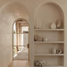 an arched doorway leads into a white room with shelves and vases on the wall