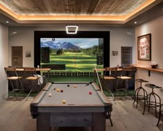 a game room with a pool table, bar stools and television on the wall