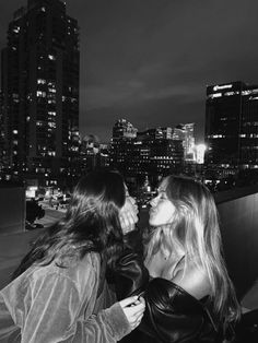 two women standing next to each other in front of a cityscape at night