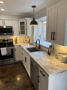 a kitchen with white cabinets and marble counter tops, stainless steel appliances and an island