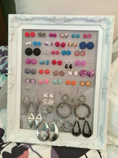 a white frame holding various pairs of earrings and earring hooks on a floral bed sheet