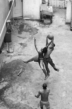 two young men playing basketball in an alleyway, one jumping to catch the ball