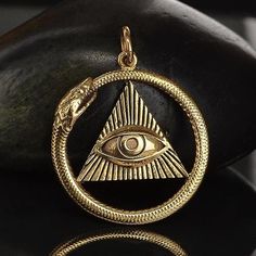 an all seeing eye pendant is shown on a black surface with a rock in the background