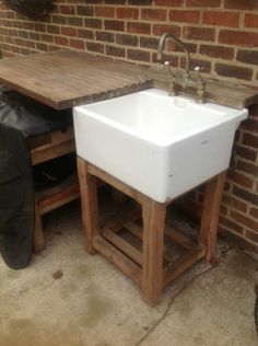 a white sink sitting on top of a wooden table next to a brick wall and trash can