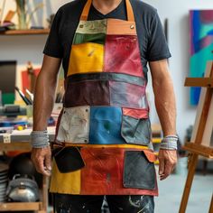 a man wearing an apron made out of multicolored leathers is standing in his studio