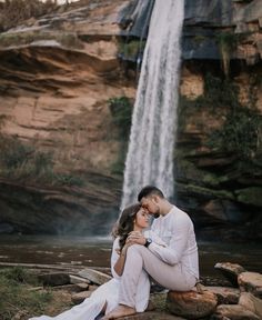 a man and woman are sitting in front of a waterfall