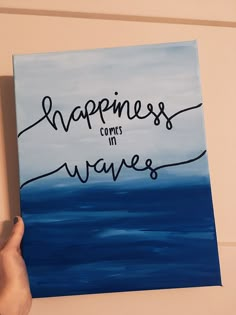 someone is holding up a painting with the words happiness comes in waves written on it