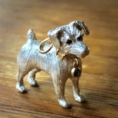 a small silver dog figurine on a wooden table with a ring around it's neck