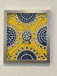 a yellow and blue decorative tile in a silver frame on a white wall with grey trim