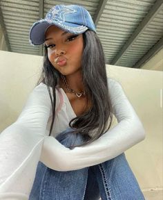 a woman sitting on top of a white couch wearing a blue hat and jeans with her tongue sticking out