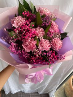 a bouquet of pink carnations and other flowers is held by someone's hand