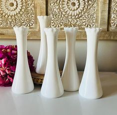 three white vases sitting on top of a table next to a pink flower arrangement