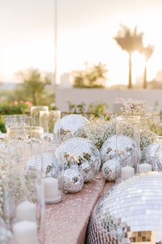 a table topped with lots of silver disco ball vases filled with flowers and candles