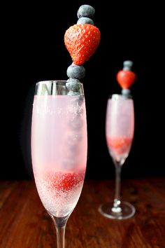 two champagne flutes with strawberries and blueberries on top, one is filled with liquid