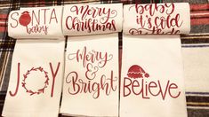 four white towels with red lettering on them sitting on a plaid cloth covered tablecloth