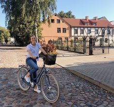 a woman riding a bike down a cobblestone road with houses in the background