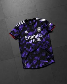 a purple and black soccer jersey sitting on top of a tile floor with the words emirates fly better printed on it