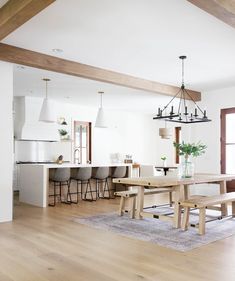 a dining room and kitchen area with wood flooring, white walls and wooden beams