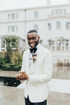 a man in a white tuxedo smiles at the camera while holding his hands together