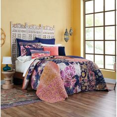 a bed in a room with yellow walls and wooden flooring that has a colorful comforter set on top of it