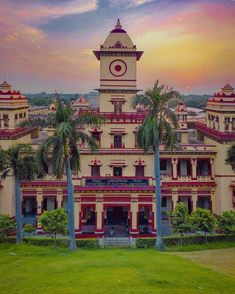 an old building with a clock tower and palm trees in the foreground at sunset