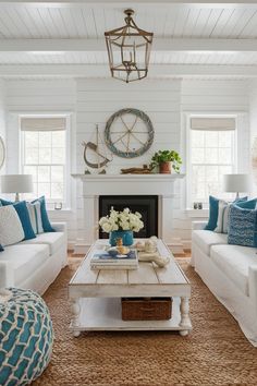 a living room with white couches and blue pillows on top of the sofas