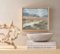 a bowl sitting on top of a wooden table next to two books and a painting