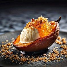 a dessert dish with ice cream and nuts on a black plate, ready to be eaten