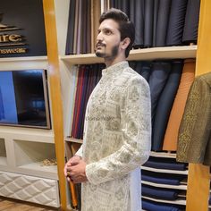 Fabric and Pattern: The sherwani is crafted from a high-quality fabric with an intricate all-over pattern of elaborate silver embellishments. The embellishments appear to be a repeating, ornamental motif that covers the entire garment, creating a visually striking and ornate appearance. Collar and Closure: The sherwani features a band collar, with a front opening secured by buttons running down the center. Sleeves: The sleeves are full-length, adding to the formal and elegant silhouette of the garment. Fit and Tailoring: The sherwani is tailored for a modern, structured fit that flatters the wearer's physique. Overall Impression: This sherwani is a true statement piece, blending traditional craftsmanship with contemporary design elements. The extensive silver embellishments and high-qualit Traditional Silver Kurta With Traditional Drape, Traditional Silver Kurta With Resham Embroidery, Silver Traditional Wear With Chikankari Embroidery, Silver Traditional Wear With Intricate Embroidery For Designer Wear, Silver Traditional Wear With Chikankari Embroidery For Weddings, Designer Silver Kurta With Zari Work, Traditional Silver Sherwani For Festive Occasions, Silver Kurta With Zari Work For Diwali, Traditional Fitted Silver Kurta