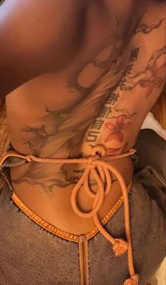 the back of a woman's body with tattoos on her chest and an orange string attached to it