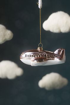 an ornament hanging from a string in the shape of a boat with clouds behind it