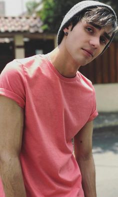 a young man in a pink shirt is holding a skateboard and looking at the camera